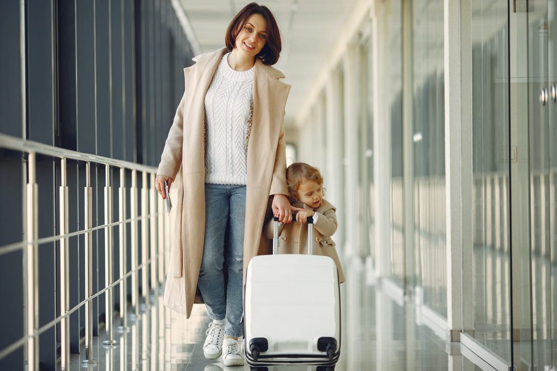 positive mother and daughter with suitcase in airport corridor